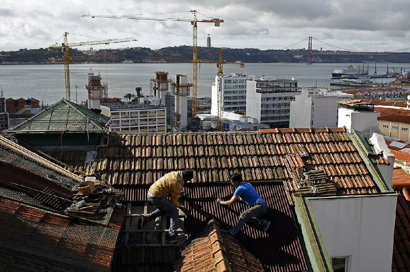Construction workers repair the roof of a building in Lisbon in this file photo from 2014. The country’s construction sector collapsed in the fi nancial crisis and has yet to recover.