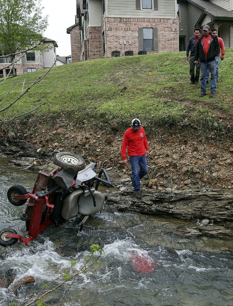 Workers with Land Design landscaping company remove a lawn mower from a creek Friday morning at Stonebridge Apartments in west Little Rock after a co-worker’s accidental death. 