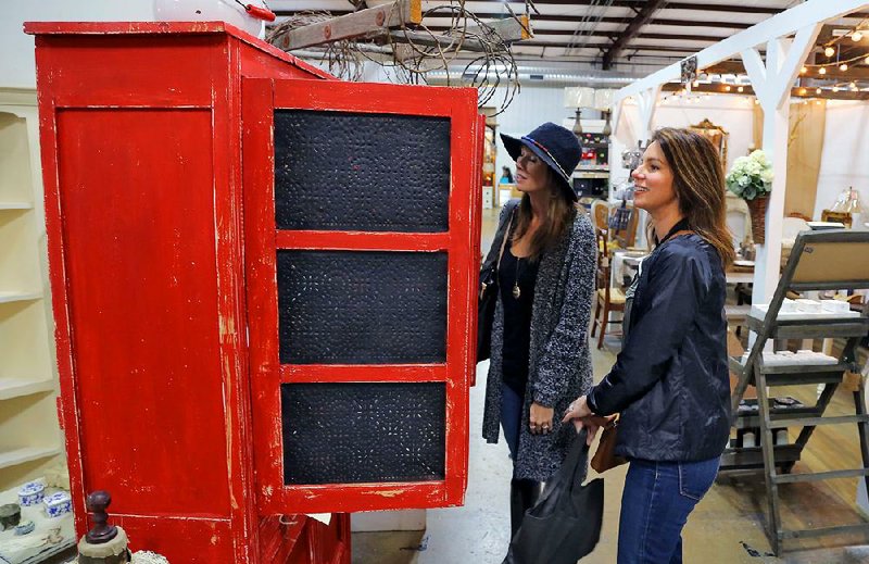 Shoppers Kimberly Hall (left) and Amanda Bass of Hot Springs check out a rustic, bright red cabinet at Painted Tree Vintage Market near Alexander. Vendors, some of whom are home interior professionals, offer items for those who want to decorate in “refined rustic” or “rustic chic.” 