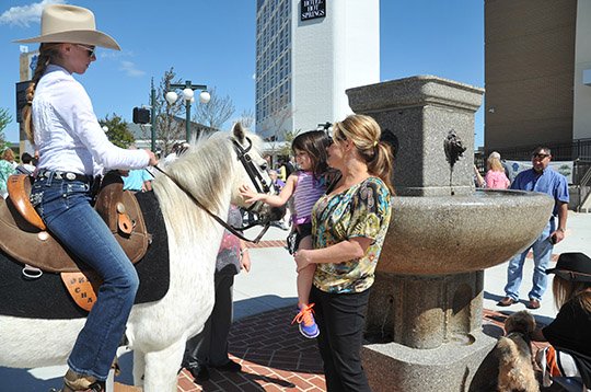 The Sentinel-Record/Mara Kuhn FIRST CUSTOMER: Donya Catlett, right, holds Ali's Angels helper Sady Bales, 4, up to pet Cowboy, ridden by Aspen Thornton, 12, who was the first horse to get a drink from the newly unveiled National Humane Alliance Water Trough Fountain at the center of Regions Plaza. The plaza and new main branch of Regions Bank were formally opened during a ceremony Thursday.