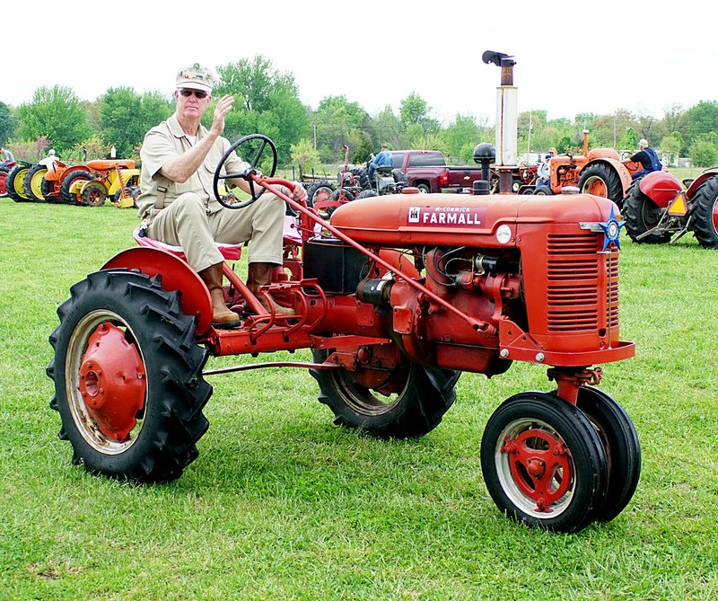 Photo by Randy Moll Glenn Smith, club member, waves as he drives an antique Farmall tractor past spectators at the 2015 spring show of the Tired Iron of the Ozarks in Gentry. Smith added an extra seat and additional controls to teach children how to drive an old tractor and to give tractor rides.