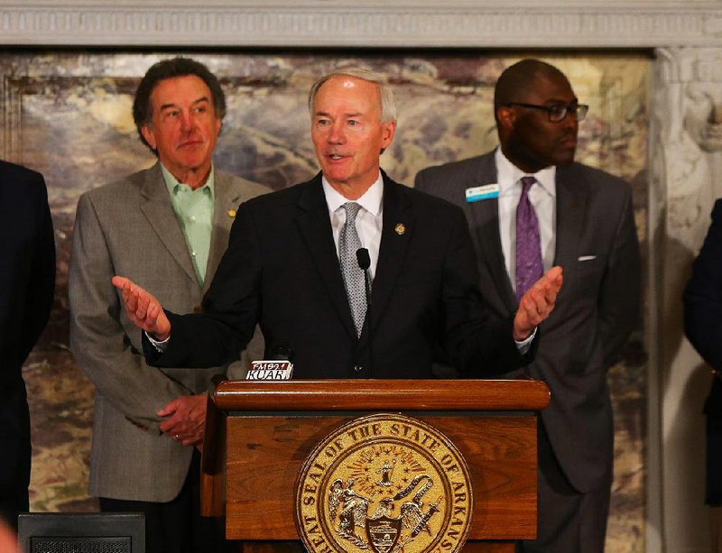 State Highway Commission members Robert Moore Jr. (left) and Frank Scott Jr. stand behind Gov. Asa Hutchinson as he issues a warning Tuesday at the Capitol about his plan to pay for highway construction. 