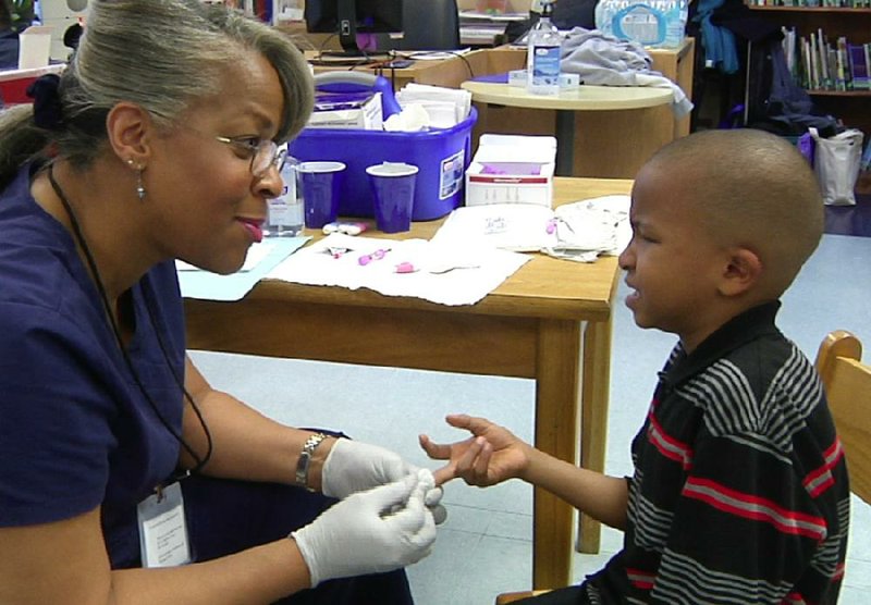 An image taken from video shows University of Michigan-Flint lecturer Veronica Robinson drawing blood from Ketisa Looney’s 7-year-old son Zyontae during a lead-testing clinic held at Richfield Public School Academy in Flint, Mich., last month.