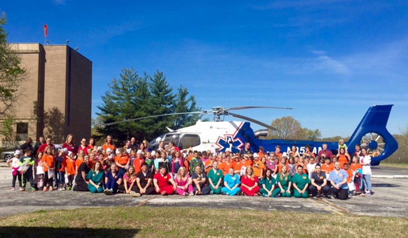 Photo by Amanda Gittlein Following the teddy bear clinic at Ozarks Community Hospital last Thursday first graders from Glenn Duffy Elementary who participated in the clinic joined OCH staff members and volunteers from Med Flight for a group photo in front of the Med Flight helicopter. The students were able to tour the helicopter and visit seven other interactive stations during the health education event, then watch the helicopter take off.