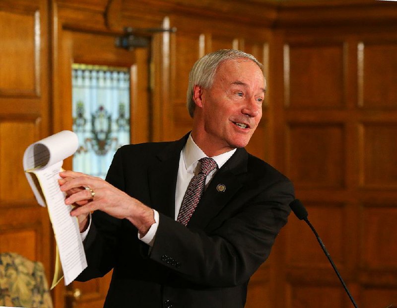 Gov. Asa Hutchinson describes the mechanics of the line-item veto as he holds the Medicaid funding bill Thursday afternoon at the state Capitol shortly after he vetoed a part of it. The bill now goes to the Senate, where opponents promise to attempt an override. 