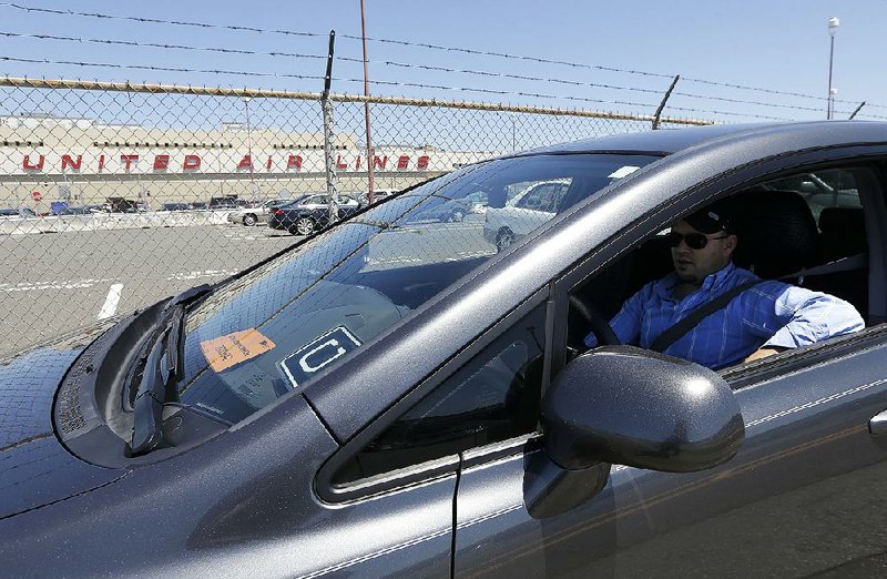 Uber driver Karim Amrani sits in his car near the San Francisco International Airport parking area in this file photo. Uber said it has reached settlements in two class-action lawsuits that allow it to treat drivers as independent contractors.