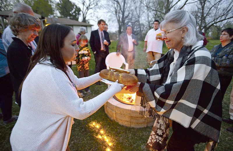 Carolyn Cole (right) of Rogers passes the challah bread to Sarah Lennick of Allentown, Pa., daughter of Rabbi Robert Lennick. Members of the congregation gathered around a backyard fire pit for fellowship and s’mores following the inaugural service April 8 at the Community Synagogue of Northwest Arkansas.