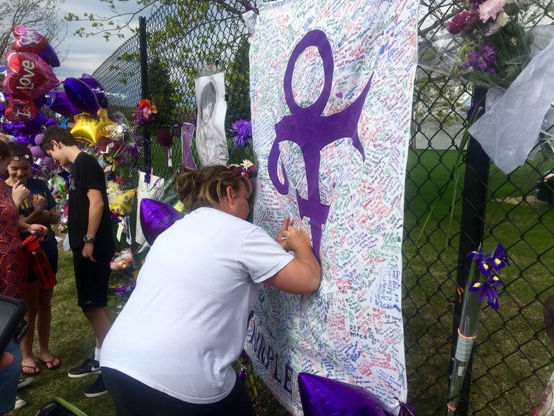 A woman writes on memorial sheet adorned with the symbol Prince once used to identify himself outside Paisley Park in Chanhassen, Minn., Saturday, April 23, 2016. The music superstar was pronounced dead at his Paisley Park estate near Minneapolis on Thursday. He was 57. (AP Photo/Jeff Baenen)