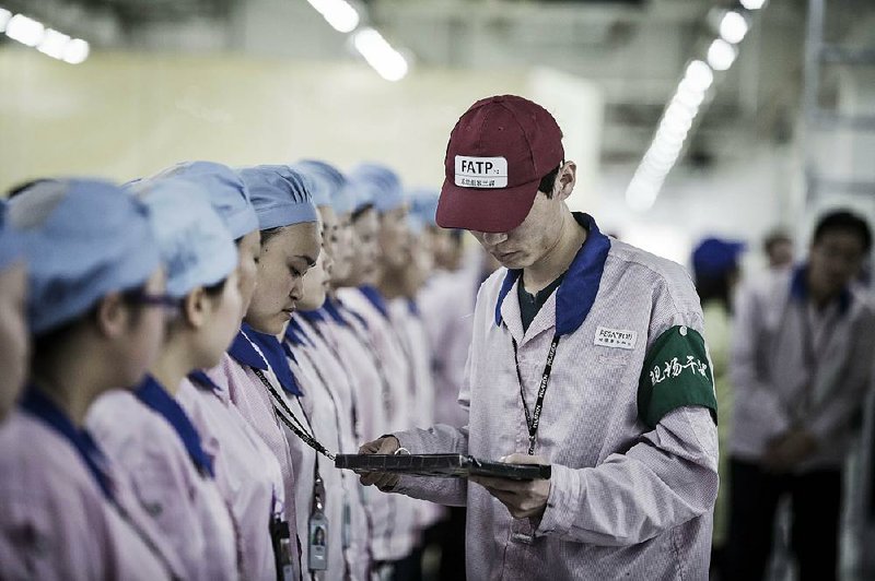 A supervisor uses an Apple Inc. iPad as he checks an employee’s badge during roll call at a Pegatron Corp. cellphone factory in Shanghai. 