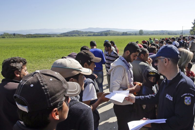 A Greek police officer hands out flyers to migrants and refugees at a makeshift camp in the northern border point of Idomeni, Greece, Wednesday, April 27, 2016. 