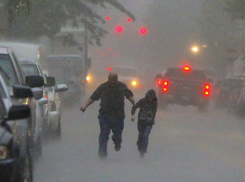 A man and a boy dash to their truck in a downpour Friday morning along President Clinton Avenue near Sherman Street in Little Rock’s River Market District as storms slammed the state.