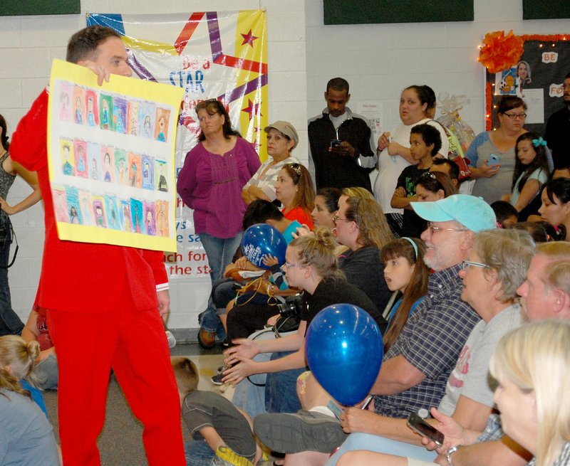 Janelle Jessen/Siloam Sunday Allen Elementary School teacher Aaron Kooistra held up a class poster as it was being auctioned to parents during Evening with the Stars on Thursday. The event served as a fundraiser for the school&#8217;s adopters and included student performances, live and silent auctions and food. The auctioning of posters created by each class has become a popular part of the event, with some posters selling for as much as $500.