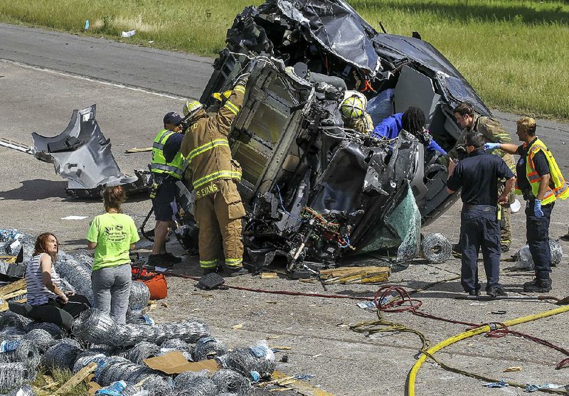 North Little Rock firefighters help the driver of a tractor-trailer (center, in blue) walk out of his wrecked cab after he crashed into the support column of the JFK Boulevard overpass over Interstate 40 while traveling eastbound on the interstate Tuesday afternoon. The truck’s cab separated from the trailer on impact and rocketed farther down the interstate. I-40 eastbound was closed during rush hour Tuesday until the truck and its load of barbed wire and metal fencing could be removed from the roadway.  