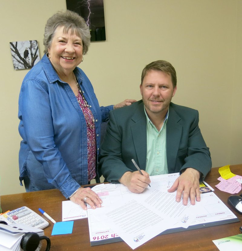 Photo by Susan Holland Mary Kay Kelley, director of the Billy V. Hall Senior Activity and Wellness Center, looked on as Gravette mayor, Kurt Maddox, signed the proclamation declaring May as Older Americans Month. Special activities are planned at the center each day during the week of May 16-20 to celebrate the month.