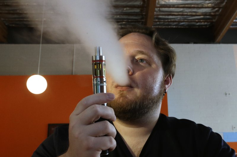 In this July 16, 2015 file photo, Bruce Schillin exhales vapor from an e-cigarette at the Vapor Spot, in Sacramento, Calif. 