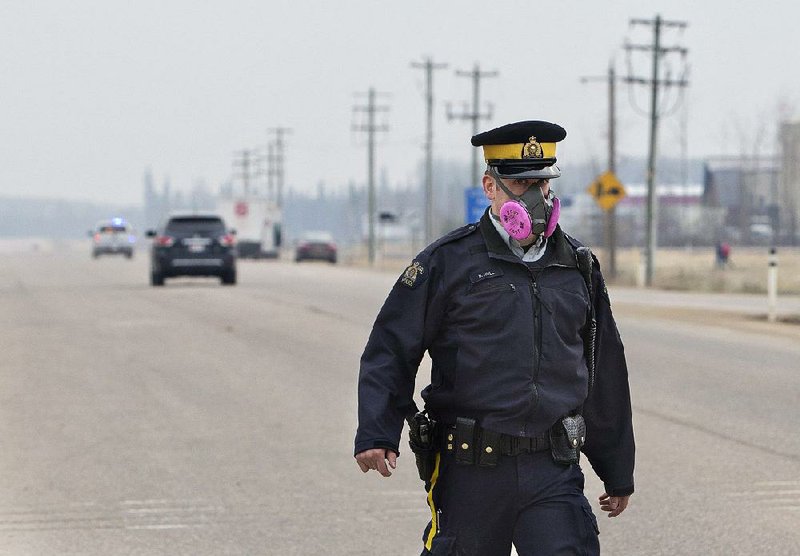 A police officer wears a mask while working at a roadblock Thursday near a wildfi re in Fort McMurray in Alberta.