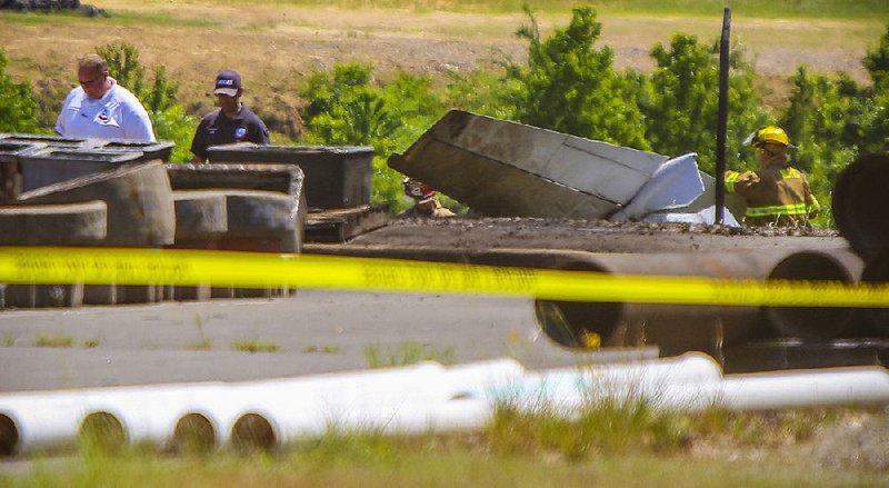 Emergency workers walk near the wreckage of a plane that crashed Thursday and caught fire, killing one and injuring another near the North Little Rock Municipal Airport. In the foreground are supplies on the ground belonging to a Central Arkansas Water facility on the airport grounds. 