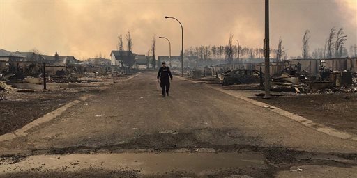 In this May 5, 2016, photo provided by the Royal Canadian Mounted Police Alberta, an RCMP officer surveys the damage on a street in fire-ravaged Fort McMurray, Alberta. 
