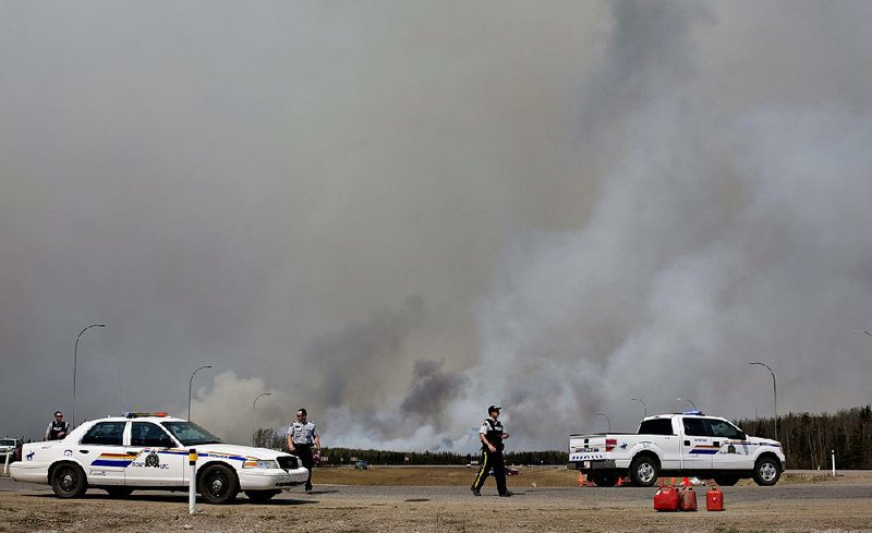 Police man a roadblock as smoke from a wildfire billows Friday in Fort McMurray, Alberta. 