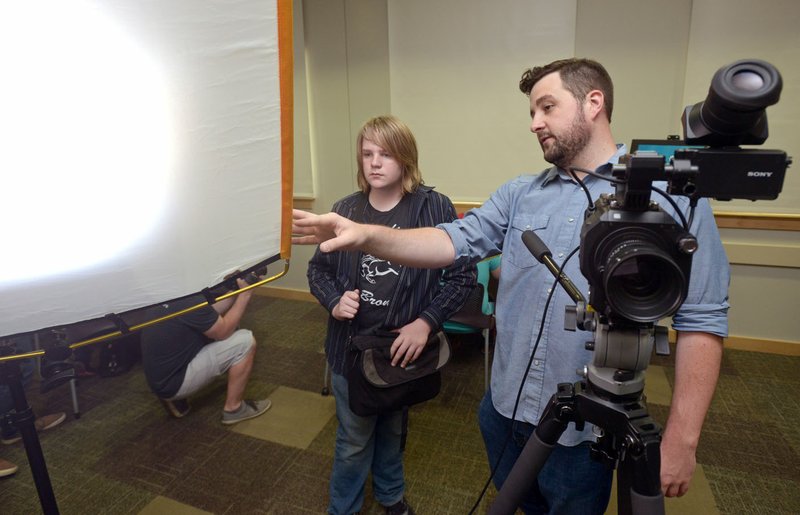 E.J. Higginbotham (right), a producer with Mitchell, talks about lighting equipment with Gray Robinson, a Fayetteville High freshman, on Saturday during the Young Filmmakers Workshop Open House presented by Mitchell at the Bentonville Public Library. The hands-on event gave aspiring young filmmakers the chance to learn about the process of making films, television and promotional videos from the professionals at Mitchell.