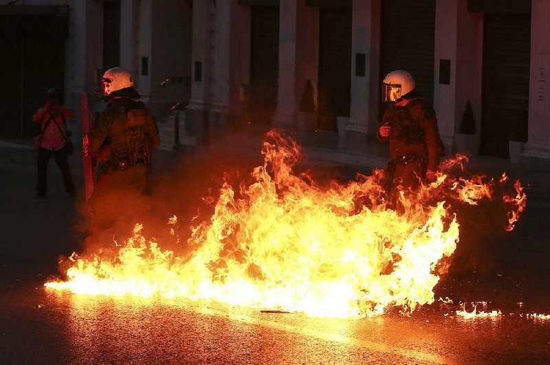 A gasoline bomb explodes Sunday in front of policemen during clashes with protesters in Athens, Greece, before a vote by Parliament on an austerity bill.