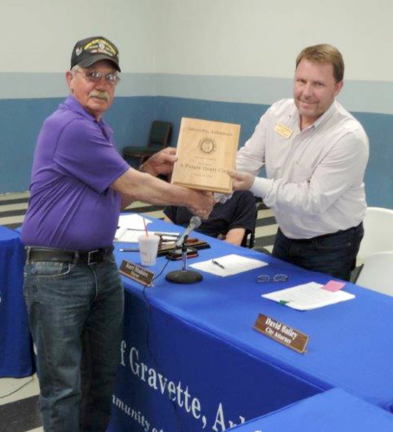 Photo by Glenn Jones Wayne Dirck, of Gravette, finance officer of Military Order of the Purple Heart Chapter 460, presented Gravette mayor Kurt Maddox the plaque designating Gravette as a Purple Heart City at the April 28 city council meeting. Following the Purple Heart City proclamation ceremony, both Mayor Maddox and Mike von Ree, city clerk, were also presented Purple Heart honor lapel pins.