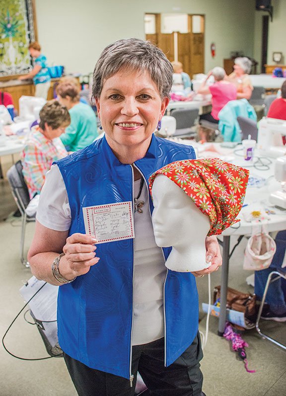 Mary Philips, founder of Care Cap Connections, holds one of the finished caps and a card that goes in each one that is sent out with the signature of every person that helped create the cap.