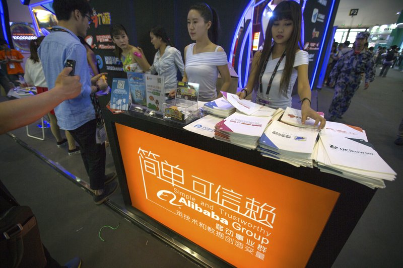 In this April 29, 2015 photo, staff members hand out brochures to visitors at the Alibaba booth at the Global Mobile Internet Conference in Beijing.  