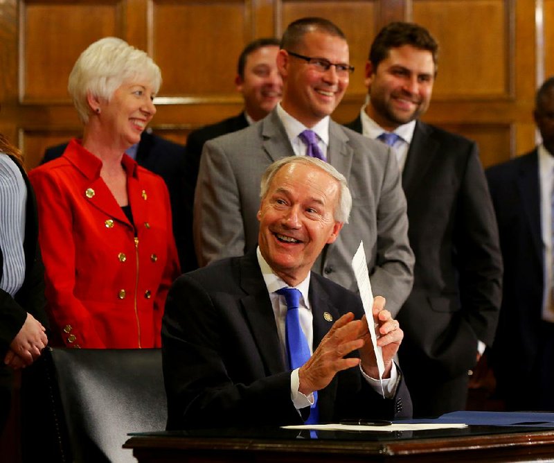 Gov. Asa Hutchinson (seated) prepares to sign a pledge Friday between the Arkansas Health Care Association and the state Department of Human Services to work out a plan to cut the state’s costs for nursing home care by $250 million over five years. 