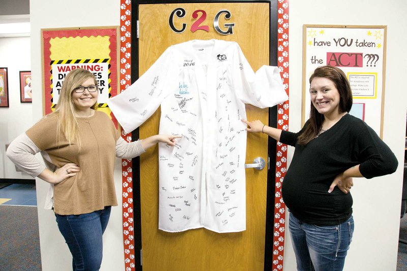 Emily McGee, left, and Kennedy Verbeck point to their signatures on a graduation gown at Cabot’s Academic Center of Excellence. Both graduated May 20 after finishing their high school careers at ACE.