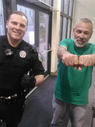 In a Saturday, May 21, 2016, photo provided by the Bangor Police Department, Bangor Police Department officer Keith Larby give a thumbs-up next to Russell Johnson, who has “Cops Suck” tattooed on his knuckles, in Bangor, Maine.