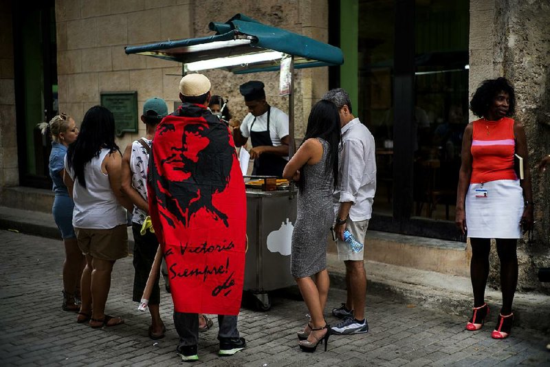 Carlo Lome Morales, a tourist from Mexico, lines up to buy churros from a street vendor in Havana on Monday. The Che Guevara flag over his shoulders says in Spanish, “To victory always.” 