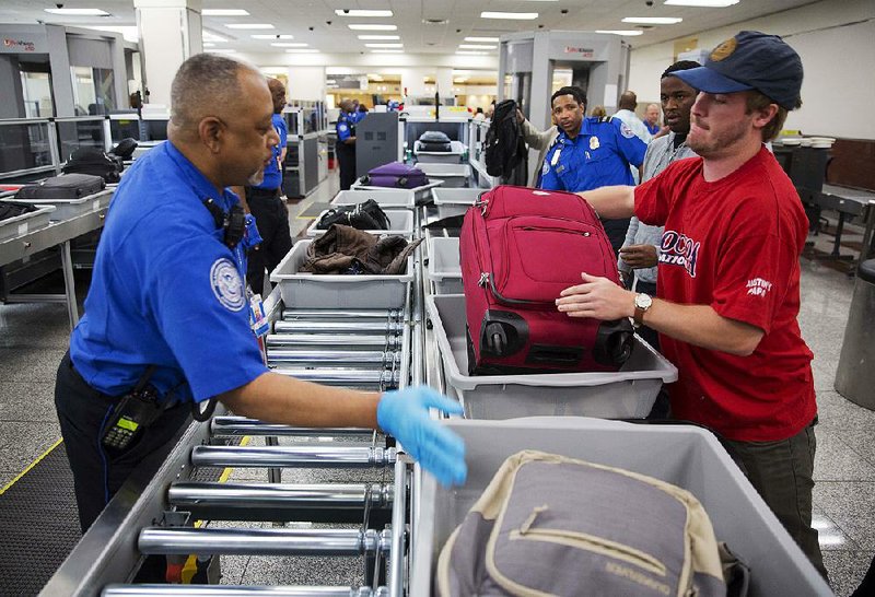 A Transportation Security Administration employee helps a passenger load carry-on luggage onto a conveyor belt at a redesigned screening lane unveiled Wednesday at Hartsfi eld-Jackson Atlanta International Airport. 