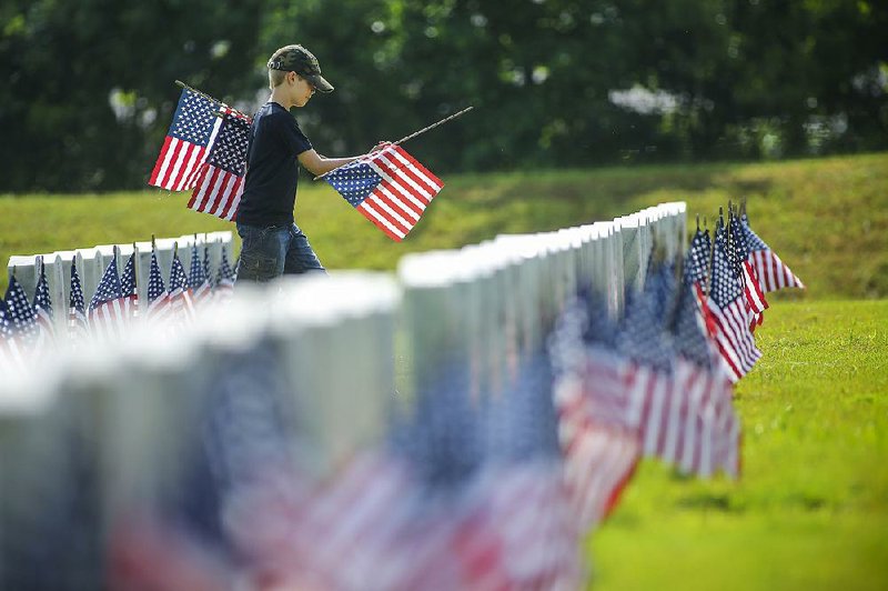 Ben Work, 9, carries American flags while working with his father, Little Rock Air Force Base Capt. Daniel Work, and a group of volunteers placing more than 6,000 flags in front of headstones Wednesday at the Arkansas State Veterans Cemetery in North Little Rock in preparation for Memorial Day. The Arkansas Department of Veterans Affairs will hold its annual Memorial Day ceremony at 10 a.m. Monday at the cemetery. 