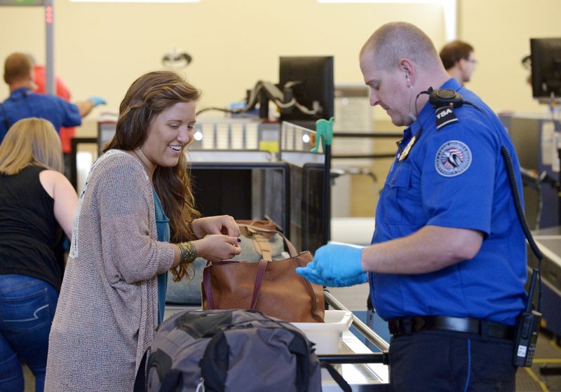 Officer Nic Vatalaro (right) with the Transportation Security Administration checks bags Thursday for Hannah Taylor as she passes through security at Northwest Arkansas Regional Airport in Highfill.