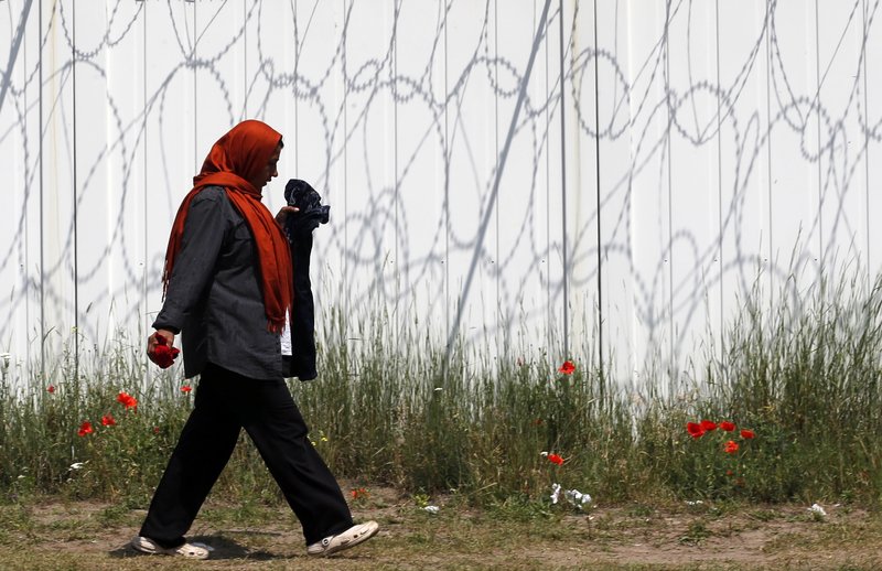 A woman walks by a border fence in the makeshift refugee camp near the Horgos border crossing into Hungary, near Horgos, Serbia, Friday, May 27, 2016. 