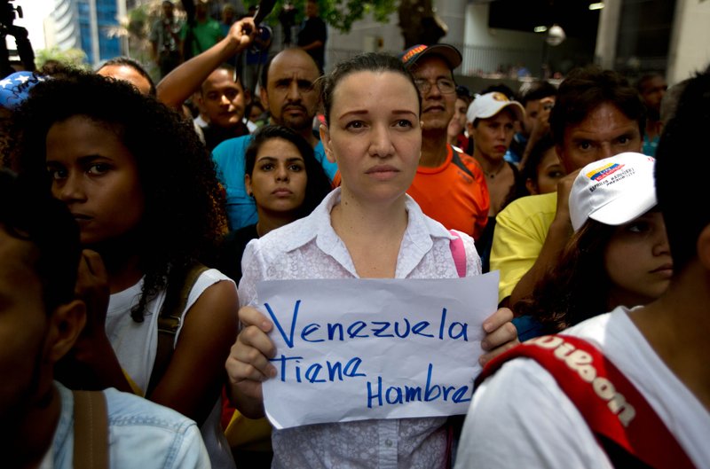 An opposition members holds a handwritten message that that reads in Spanish; "Venezuela is hungr" during a protest outside the court offices of the Chacao municipality, in Caracas, Venezuela, Wednesday, May 25, 2016. 