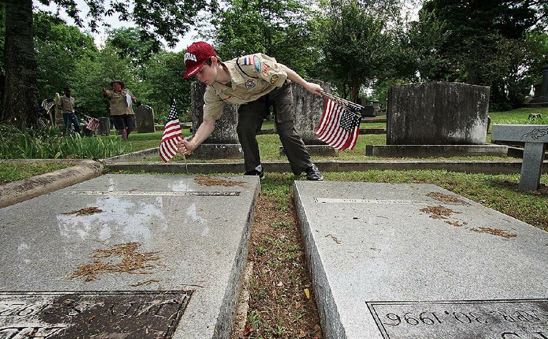 John Smith, 13, of Mabelvale plants flags Sunday at Mount Holly Cemetery in Little Rock next to the graves of those who served in the armed forces.