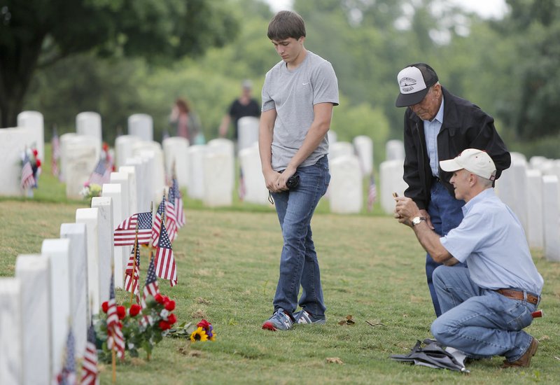 Clay Metz (left), 16, of London, stands Monday with his father, Charlie Metz (right), and his grandfather T.A. Metz, a WWII Navy veteran, as they visit the grave site of a relative following the Memorial Day ceremony at Fayetteville National Cemetery.