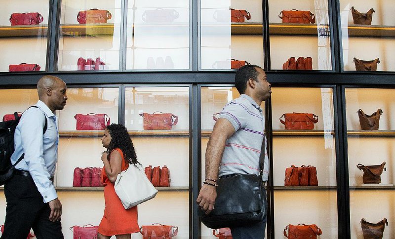 People pass displays of Coach handbags Tuesday as they walk through the lobby of the company’s new headquarters at 10 Hudson Yards in New York. Coach is the anchor tenant in the office tower on Manhattan’s west side. 