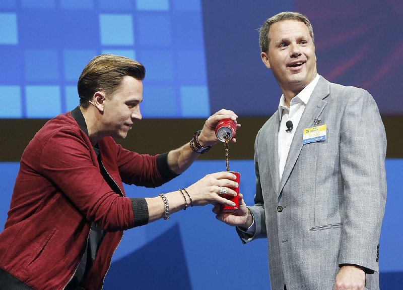 Justin Flom (left), assisted by Wal-Mart Inc. President and CEO Doug McMillon, performs a magic trick with a soft drink Wednesday during the retailer’s annual shareholder meeting in Fayetteville.