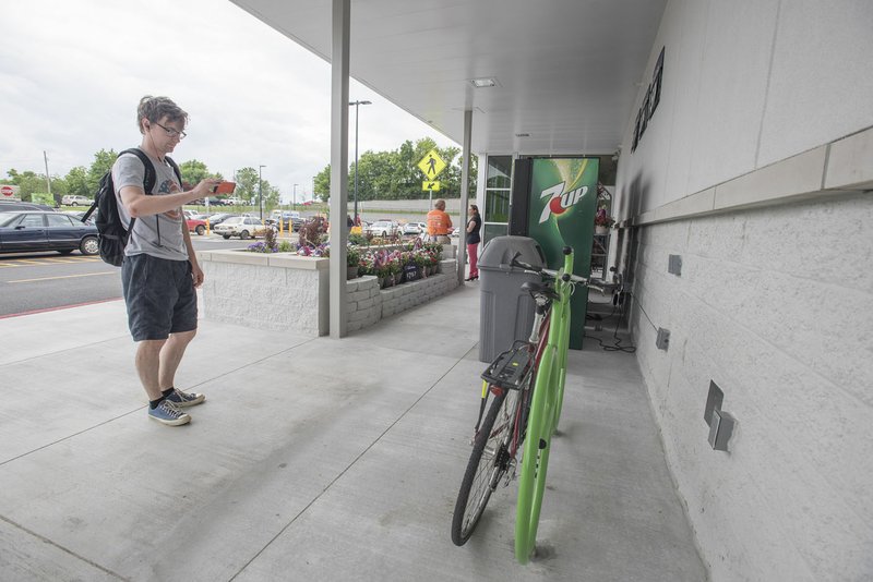 Dimitry Kislitsyn photographs his bicycle chained to a rack shaped like a bicycle Thursday before shopping at the Wal-Mart Neighborhood Market on Martin Luther King Boulevard in Fayetteville. Kislitsyn, a University of Arkansas student, lives in the neighborhood close by.