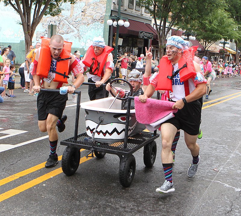 The Sentinel-Record/Richard Rasmussen WATER HAZARD: Members of the Riser Auto Tub team, from left, Clay Shatley, John Ringgold, Matt Barrett, in tub, Evan Dingler, right, and Tex Holmes, not visible in back, roll across the finish line to win the Traditional Tub division of the 11th Annual Stueart Pennington Running of the Tubs Saturday.