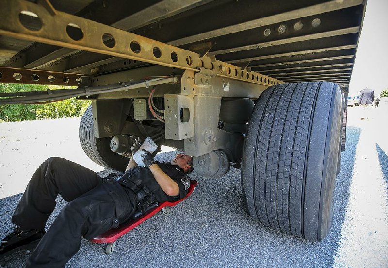 Arkansas Highway Police Cpl. Kreston Taylor rolls beneath a tractor-trailer rig on an automotive creeper as he inspects the truck as part of the 2016 International Roadcheck on eastbound Interstate 30 just west of Benton on Tuesday morning. 