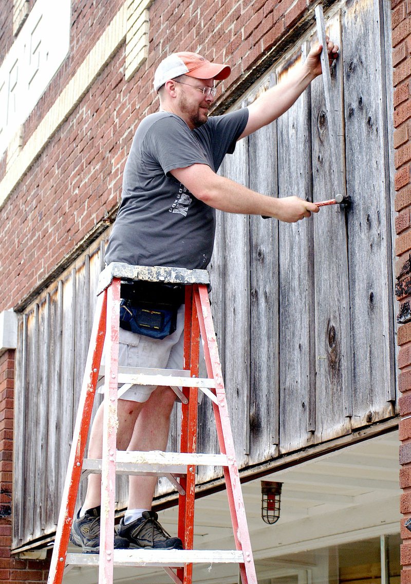 Photo by Randy Moll Charlie Bookout removes the wooden planks covering the windows on the Carpenter Building on Main Street in Gentry Thursday morning, revealing the restored original windows of the 1929 building which once housed a grocery and furniture store and mortuary.