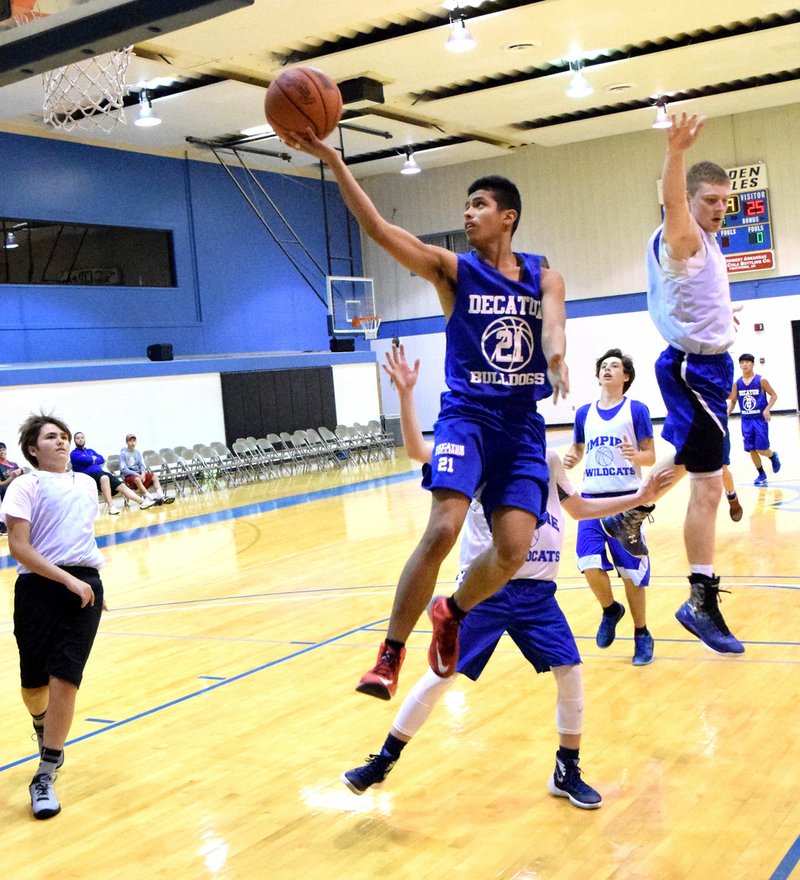 Photo by Mike Eckels Jimmy Mendoza, Bulldogs #21, slips past a group of Wildcats for a layup during the Decatur-Umpire basketball game at John Brown University&#8217;s team camp in Siloam Springs June 3.