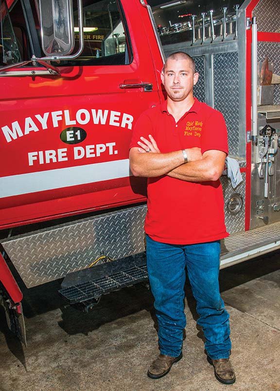 New Mayflower Fire Chief Josh Woods stands by one of the firetrucks in the volunteer department. He was hired May 20 and will oversee 14 volunteers, he said. Woods has lived in Mayflower for 10 years and has been a volunteer firefighter there for a year. He also has experience working in the Centerton, Sherwood and Maumelle fire departments.