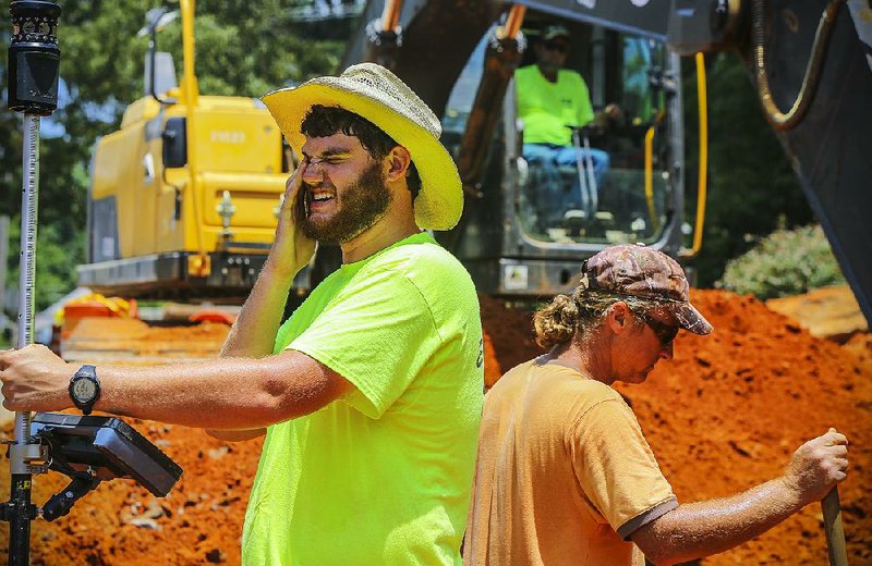 John Helmich (left) wipes sweat from his eyes Thursday as he and Denver Bunt (right), both with H&H Excavating of Alexander, work to rebuild Lillian Street from East North Street to East Sevier Street in Benton.