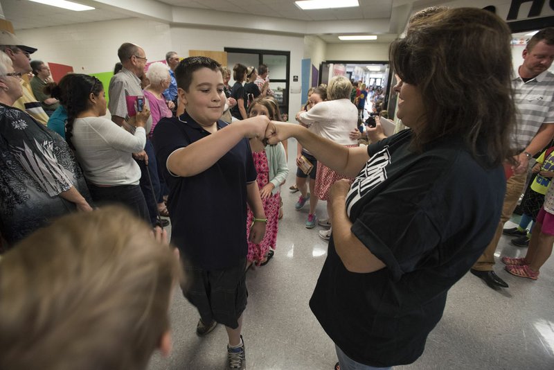 Elm Tree Elementary School fourth-grader Dominic Vernetti bumps fists with kindergarten teacher Dena Chambliss on Thursday during the traditional fourth-graders walk through the halls on the last day of school. Thursday ended the year for the nontraditional calendar schools, Baker Elementary School and Elm Tree, both of which will return to a regular calendar with the rest of the Bentonville schools next school year.