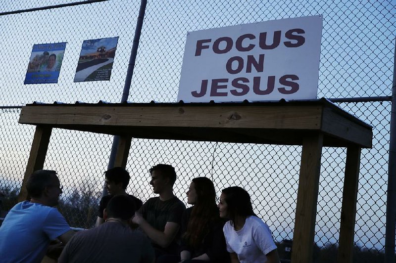 Youths sit under a sign at a baseball field in the gathering dusk outside the evangelical Christian Fellowship Church in Benton, Ky. 